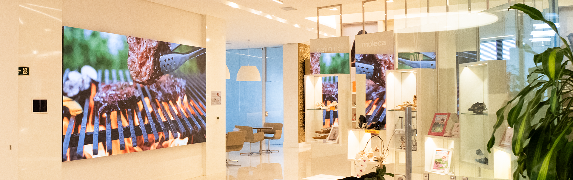 Painel de LED indoor instalado pela IDEA Painéis de LED na Calçados Beira Rio, exibindo conteúdo em alta definição em ambiente corporativo moderno, com vitrines de produtos e comunicação visual de alto impacto.